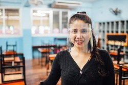 Portrait of beautiful Asian female teacher wearing face shield smiling while standing  in classroom. New normal lifestyle during corona virus or Covid-19 crisis