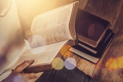 Close up of a woman hand  hold and reading the open bible, blurred page on wooden table with window light and Bokeh, Christian devotional, spiritual or bible study concept background with copy space