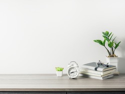 Workspace with book, clock and tree pot on wood table with living room white wall