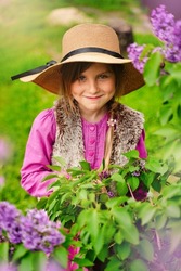 Portrait of sneaky scheming little girl in casual wear thinking over cunning prank and smirking, disobedient child having sly tricky plans in mind. Outdoor garden shot purple background