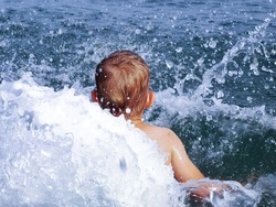 Toddler boy jump in water. Splash of water around of child. Jumping playing in blue sea. 