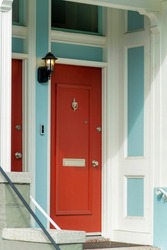 Red front door on modern doorstep in the neighborhood in downtown major city with white accent paint and blue. In sun in late afternoon house access with stairs and hand rail.