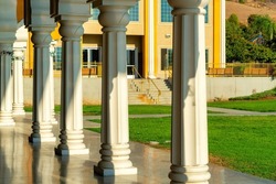 white middle eastern architectual pillars in late afternoon sun and walkway with some shade and green lawn with building and tree background