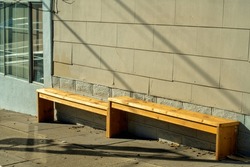 Hillside bench with uneven legs for passersby and pedestrians to sit and rest in modern downtown city neighborhood. Wooden exterior with shadows and sun and brick building background.