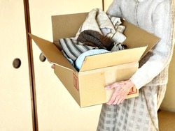 Hands of an elderly woman holding a cardboard box containing clothes