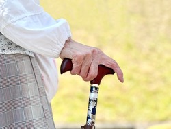 Hands of an elderly person with a cane in lawn background