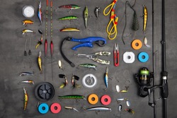 Fishing tackle - fishing spinning rod, hooks and lures on gray background. Active hobby recreation concept. Top view, flat lay.