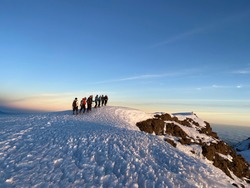 Group of hikers reaching the top of Kilimandjaro at sunrise with clear blue sky and walking on snow