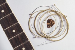 Acoustic guitar strings, pick and guitar neck on gray paper background