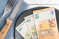 Conceptual studio shot of dinner table with euro bank notes on the plate instead of food. Concept for rising food prices, inflation, economic crisis, consumer prices index.