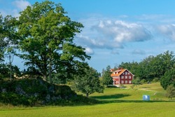 Typical red wooden houses in countryside by the sea in nature of southern Sweden on a beautiful sunny summer day. White heystacks in front. Relaxing rural landscape.