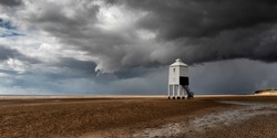 The low lighthouse on Burnham-on-Sea beach with dark brooding stormy clouds but with sunlight streaming in from the left hand side