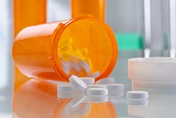 Healthcare and medical concept - orange prescription bottle with pills and drugs in the hospital. Glass tabletop with reflections in sterile room. Close up view