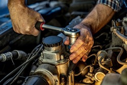 Repairman's male hands with a wrench. Vehicle fitter inspecting used car engine. Car components, belts, hoses, labor arm close up in the open hood of the car. Service center, auto repair shop