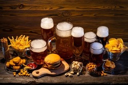 Glass of beer on bar counter. Jugs, mugs, pints of brew beverage, ale, cider on wooden table in pub, bar. Backlit dark showcase with craft beer bottles in brewery. French fries fried potatoes snack.