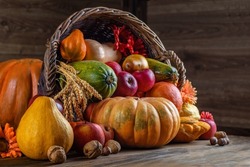 Thanksgiving day close up still life. Pumpkin harvest in wicker basket. Squash, vegetable autumn fruit, apples, and nuts on a wooden table. Halloween decoration fall design.