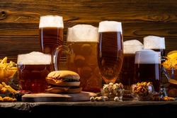 Glass of beer on bar counter. Jugs, mugs, pints of brew beverage, ale, cider on wooden table in pub, bar. Backlit dark showcase with craft beer bottles in brewery. French fries fried potatoes snack.
