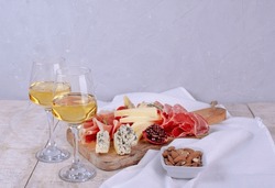 Mixed delicatessen and white wine with charcuterie and cheese board . Space for banner, logo, copy space. Italian appetizers or antipasto set with gourmet food on table