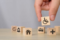 hand picking up wooden block with icons related to disability, medical, rehabilitation service, nursing care. can use for medical and rehabilitation concept article, banner, brochure in handicap.