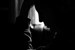 Monochrome photo of a depressed man silhouetted by the light of a window and holding his head in his hands