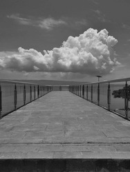 A long pier with a cloudy sky in the background - black and white photograph.