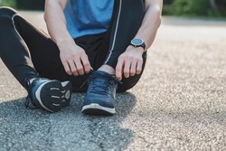 Young male in sportswear tying shoelace in the park outdoor, athlete runner man ready for running and jogging in morning. Exercise, wellness, healthy lifestyle and workout concept