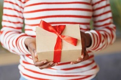 african American woman gives or receives a gift. a happy millennial woman with a cardboard box and a red ribbon in her hands. an anniversary and birthday gift for a friend or wife. party joy and