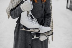 young European woman in winter clothes is skating, lady with red hair is wearing white skates on a snow rink in park. happy millennial woman is having fun. winter christmas holidays