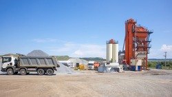 The territory of the asphalt plant during working hours. Dump trucks are waiting for their turn to be loaded on the territory. Sunny, clear summer day at the factory.