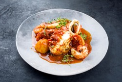 Traditional Brazilian fish stew moqueca capixaba with fish filet and king prawns in tomato sauce as closeup on a modern design plate 