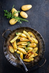 Traditional roast potatoes with herbs offered as top view in a rustic wrought- iron pan