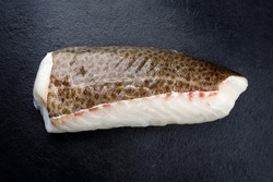 Raw Norwegian skrei cod fish filet with skin as closeup on black board with copy space 