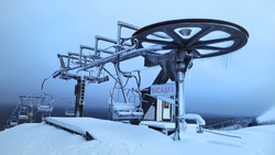 A frozen and abandoned Chairlift in the snowy mountains. A devastated ska lift covered with snow and frost with a red inscription 