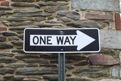 A oneway street sign against a stone wall. 