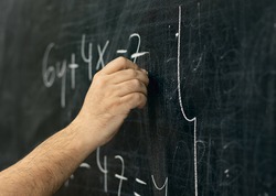 Close-up shot of a hand holding chalk and writing mathematical equations on the blackboard.
