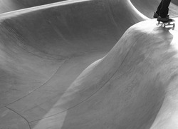 Minimalist, black and white photograph shows curves of skate park and movement of rider's feet and skateboard.