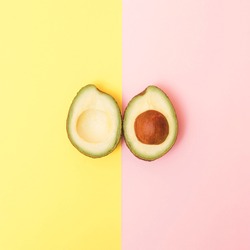 Two upsidedown  halves of avocado on a pastel yellow and pink background.