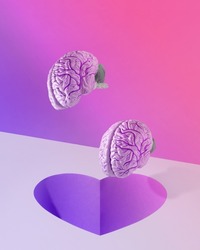 Brains fall into a heart-shaped hole on a gradient background. Surreal minimal abstract concept of falling in love, loving couple, romance or lovers. Purple and pink lights. Valentine’s Day card idea.