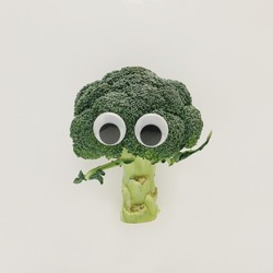 Funny face made of green broccoli and big eyes on isolated pastel beige background. Minimal abstract creative concept of healthy vegetable or agriculture. The idea of  eating natural raw organic food.