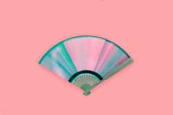 Top view of compact disc made fan with rainbow reflections on isolated pink background. Creative, retro, abstract, music concept. Light diffraction into iridescent pink-blue-purple-green spectrum.