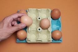 Eggs in an egg carton with orange background, hand giving one egg