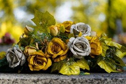 A wreath of artificial roses in gold and silver, placed on the grave. Autumn bokeh background.                               