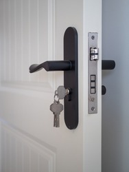 There is a black door handle on the white wooden door with a key inserted in the keyhole