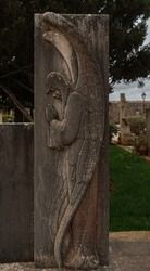 Statue of an angel with wings praying in a cemetery