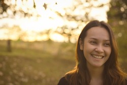 Front view of young woman warm smile with bokeh in golden hour
