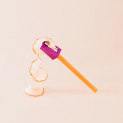 Creative composition made of orange pencil and purple pencil sharpener against a bright beige background. Minimal back to school concept.