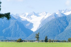 Beyond green farmland to foothills of Southern Alps and the popular tourist attraction of Fox Glacier, South Island New Zealand.