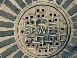 Grimy sewer manhole cover in city street in monochrome.