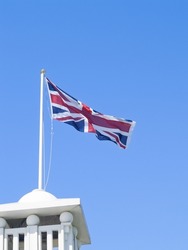 Union Jack fluttering in breeze from pole on turret against blue sky.