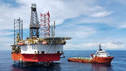 A jack up rig with an anchor handling vessel during cargo operation at sea.